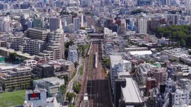 Tokyo, Japonya 'nın geniş hava manzarası, Tokyo Kulesi, bir demiryolu hattı, ve berrak mavi gökyüzü altında modern ve geleneksel binaların karışımı..