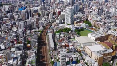 Tokyo, Japonya 'nın havadan görünüşü, Shinjuku gökdelenleri, bir demiryolu hattı, yeşillik ve dağınık bulutlu mavi gökyüzünün altında bir spor sahası..