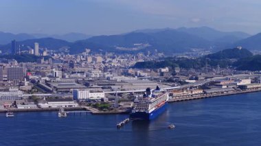 Japonya 'nın Hiroşima şehrinin havadan görünüşü modern binaları, yeşil dağları, sakin bir rıhtımı ve yavaş hareket eden rıhtımlı tekneleri gösteriyor..