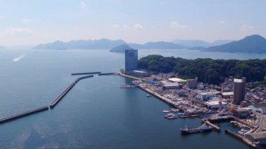 Japonya, Hiroşima 'nın sakin hava manzarası, yeşil tepeleri, sakin bir denizi, hareket eden bir tekneyi, dalgakıranı, uzak dağları ve kırmızı bir şanzıman kulesini gösteriyor..