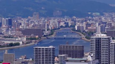 Hiroşima şehrinin hava manzarası, modern binaların sergilenmesi, köprülü Ota Nehri, ve arka planda yavaş çekim panelli yeşil tepeler..