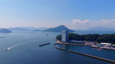 Japonya 'nın Hiroşima kentsel binaları, yeşillikleri, sakin suları, dalgaları ve uzak endüstriyel vinçleri olan kıyı bölgesini gösteren hava manzarası..