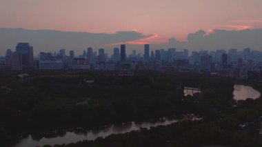 Osaka Kalesi 'nin havadan görünüşü yeşillik ve hendekle çevrili, şehrin ufuk çizgisi ve arka planda günbatımı renkleriyle. Yavaş yavaş dışa doğru hareket.