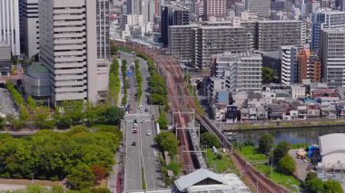Japonya 'nın Osaka kentinin havadan görünüşü, yüksek binalar, yerleşim alanları, tren rayları üzerinde hareket eden trenler ve açık bir gökyüzünün altındaki dağlar gösteriyor..