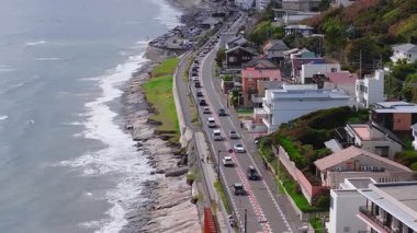 Japonya 'daki Kamakuro şehrinin hava görüntüsü, eğimli bir kıyı şeridi, hareket eden araçlar, yamaçtaki evler, yemyeşil alanlar ve okyanus dalgalarını gösteriyor..