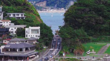 Japonya 'daki Kamakuro şehrinin hava manzarası, yeşil tepeler, dar bir yol, modern ve geleneksel binalar ve küçük yelkenli tekneli bir körfez gösteriyor..