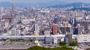 Japonya 'nın Hiroşima şehrinin havadan görünüşü, modern binaları, köprüleri olan bir nehri ve arka planda yavaş çekim ile yemyeşil dağları gösteriyor..