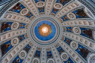 Frederik Kilisesi 'nin kubbesinde altın bir güneş patlaması, mavi arka plan, detaylı freskler, dini figürler ve karmaşık dekoratif desenler bulunur..