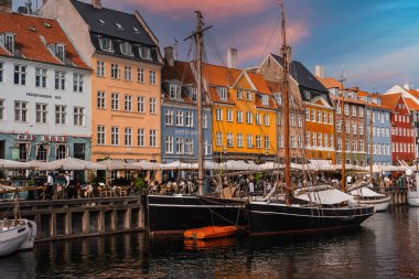 Canlı binalar Kopenhag, Danimarka 'daki Nyhavn Kanalı' nda tarihi ahşap gemiler, açık hava kafeleri ve sıcak bir günbatımı gökyüzü ile canlı bir sahne yaratıyor..