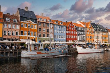 Danimarka 'nın Kopenhag kentindeki Nyhavn bölgesinde altın saatinde canlı tarihi binalar, rıhtımlı tekneler ve sakin bir kanal boyunca uzanan açık hava koltukları bulunmaktadır..