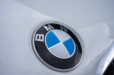 Mavi ve beyaz kadranlı BMW logosu beyaz bir BMW X6 'nın kaputunda gösterilir, gökyüzündeki hafif ışık ve soluk bulutları yansıtır..