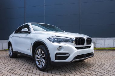 Asfaltlı bir yüzeyde beyaz bir BMW X6 'nın yakın görüntüsü, böbrek ızgarasını, keskin farlarını ve arkasında gri bir bina bulunan spor kıvrımlarını vurguluyor..