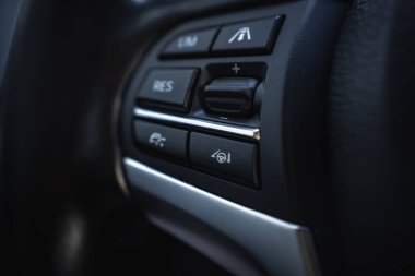 BMW X6 direksiyon simidindeki kontrol düğmelerinin detaylı görüntüsü, siyah ve gümüş bir dizayn ile yol kontrolü ve şerit desteği.