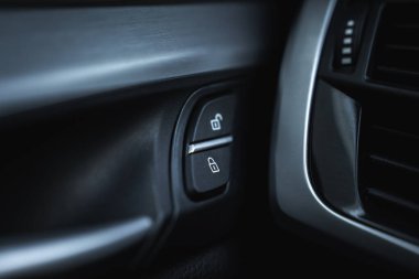 BMW X6 'nın iç görüntüsünü kapat. Metalik aksanlı siyah paneldeki kapı kilidi düğmelerini ve gümüş bukleli havalandırma deliğinin bir kısmını göster..