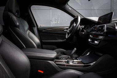 Siyah deri koltukları, karbon fiber aksanları olan bir BMW X4 'ün iç görüntüsü, dijital bilgi ekranı, ve kapalı alanda parlak bir merkez konsolu..