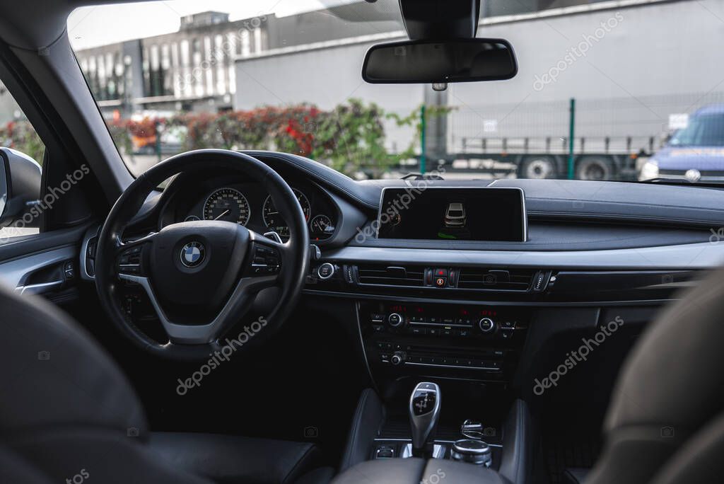 Close view of BMW X6 interior showing digital dashboard, steering wheel with BMW logo, gear selector, and an urban setting outside the vehicle.