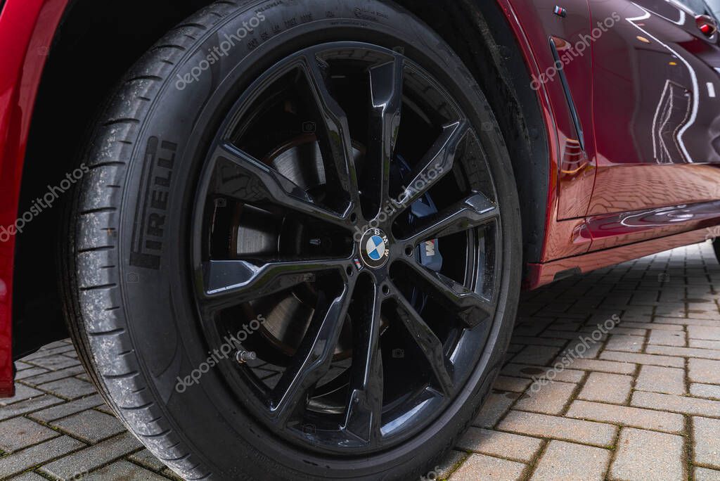 Close up view of a BMW X4 wheel featuring a glossy black alloy rim with BMW logo, Pirelli tire tread, and red car body on interlocking brick pavement.
