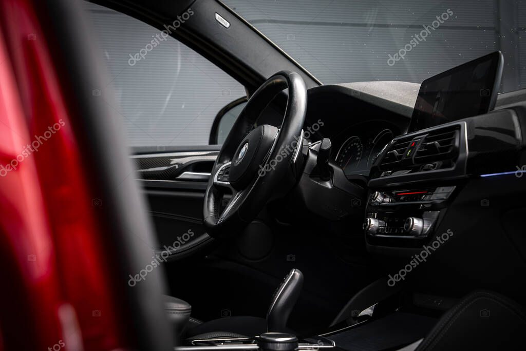 Close up view of the BMW X4 interior showing the steering wheel with BMW logo, digital dashboard, and sleek black design. Red exterior partially visible.