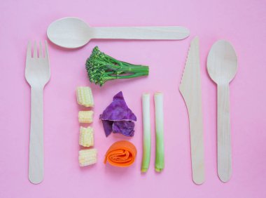 Bir düz taze sebze ve vegan veya vejetaryen gıda çevre dostu ahşap çatal bıçak takımı pembe bir arka plan üzerinde hafif bir öğle yemeği için hazır bir yer ortamda yatırın