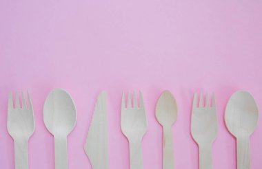 A flat lay of a variety of sustainable and environmentally friendly wooden cutlery including knife, fork and spoon with copy space on a pink background