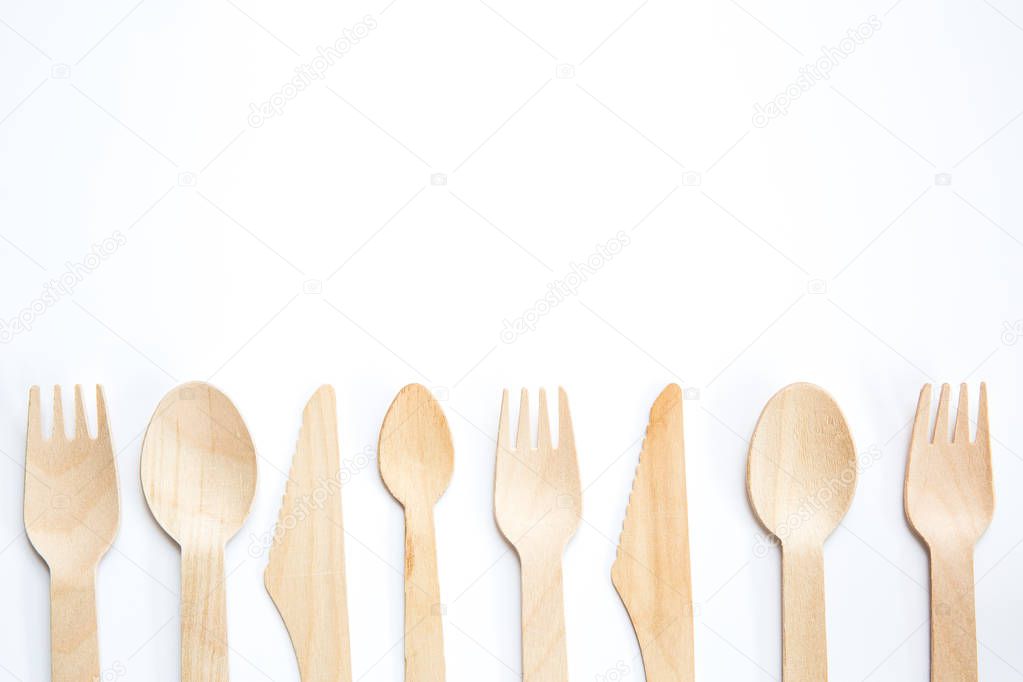 A flat lay of a variety of sustainable and environmentally friendly wooden cutlery including knife, fork and spoon with copy space on a white background