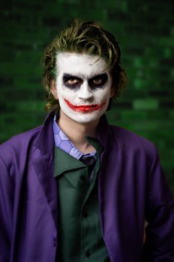 Joker gibi giyinmiş, gülümseyen ve fotokopi aletiyle kameraya bakarken eğlenen genç bir erkek oyuncunun portresi.