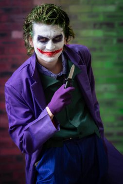 Joker gibi giyinmiş, gülümseyen ve fotokopi aletiyle kameraya bakarken eğlenen genç bir erkek oyuncunun portresi.