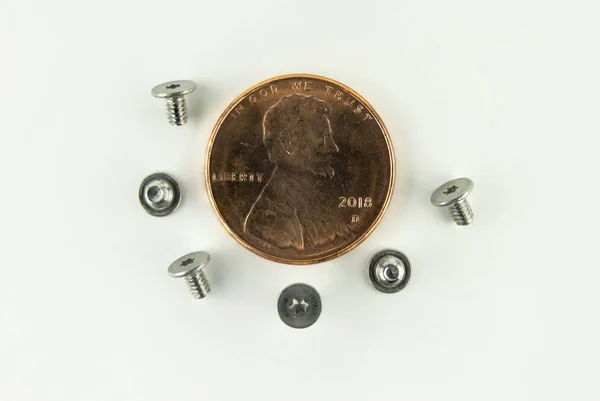 从电脑硬盘上取出6个小小的银色 Torx 或星头螺丝 并在一分铜币周围排起了长队 以进行尺寸比较 — 图库照片