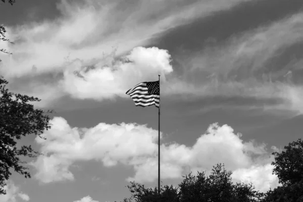 US Flag waving above trees on cloudy sky