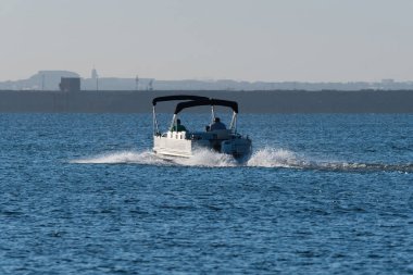 İkiz tepe örtülü Pontoon teknesi, sabahın erken saatlerinde güneşin sıcacık parıltısıyla gölde bir günlüğüne yola çıkıyor..