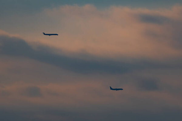 Пара пассажирских самолетов, летящих по облачному, пасмурному небу, как ранний утренний восход солнца бросает теплое свечение на облака.
