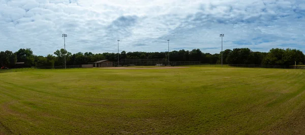 A panoramic view of an empty baseball field in a city park looking toward home base from centerfield on a cloudy, overcast summer day.