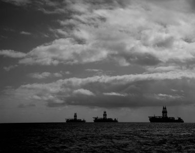 Arkadan aydınlatmalı petrol platformları ve şafak vakti bulutlu gökyüzü, siyah ve beyaz