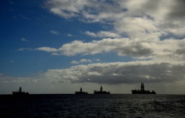 Petrol platformları koyda demirledi, şafaktan sonra bulutlu gökyüzü ve sakin deniz