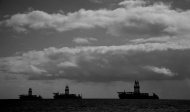 Arkadan aydınlatmalı yağ platformları, bulutlu gökyüzü ve şafak vakti sakin deniz, tek renkli mod