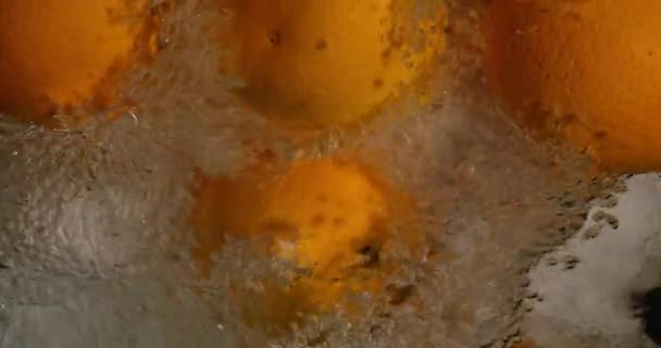 Gocce arancioni sott'acqua su sfondo nero. Frutta fresca arancione che si tuffa e schizza acqua. Bolle d'aria dell'acqua — Video Stock