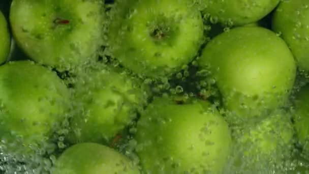 Gröna äpplen faller ner i vatten mot svart bakgrund, super slow motion — Stockvideo