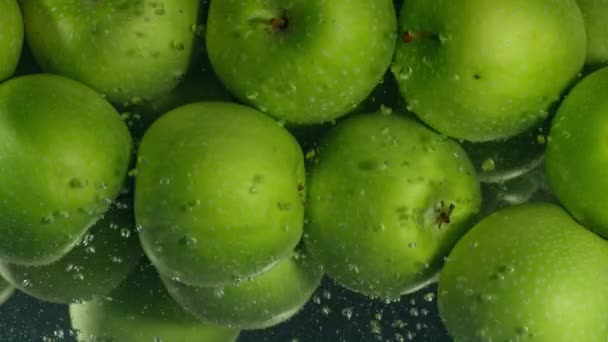 Gröna äpplen faller ner i vatten mot svart bakgrund, super slow motion — Stockvideo