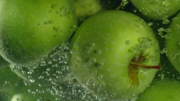 Green apples fall down in water against black background, super slow motion — Stock Video
