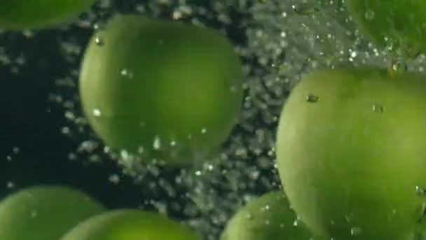 Mele verdi cadono in acqua sullo sfondo nero, super slow motion — Video Stock