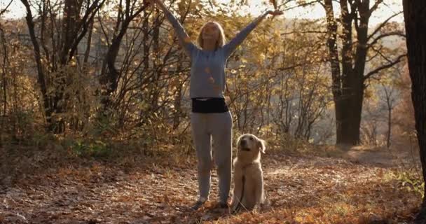 Νεαρή γυναίκα με το σκυλί retriever πετώντας μέχρι φύλλα το φθινόπωρο δασικό πάρκο — Αρχείο Βίντεο