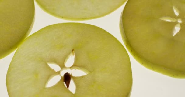 Rodajas de manzana verde girando sobre un fondo blanco brillante. Vista de cerca, filmada con la cámara RED 6K — Vídeos de Stock