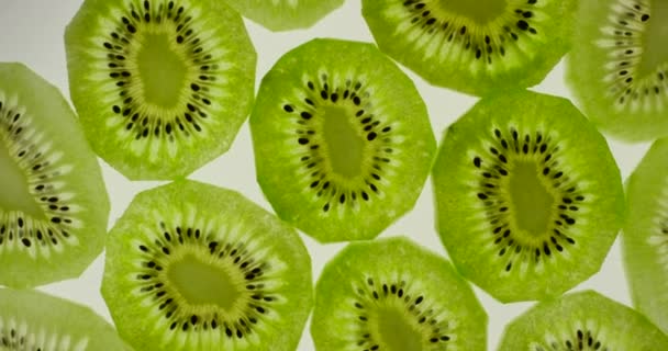 Kiwi-Fruchtscheiben rotieren auf einem strahlend weißen Hintergrund. Nahaufnahme von oben, aufgenommen mit roter 6k-Kamera — Stockvideo