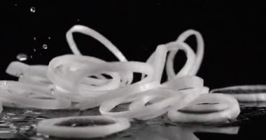 Beyaz soğan halkaları siyah arka planda yavaş çekimde düşüyor. Yakın çekim, kırmızı 6K kamera.