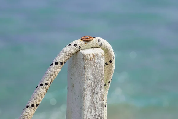 Corda legata ad un palo di legno, dettaglio con montante sul molo del mare vite arrugginita. Da vicino. — Foto Stock