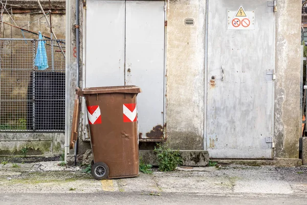 brown garbage bin in the back of an urban street area .