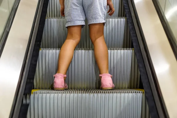 young female kid on a moving escalator . Do not let a child go alone on an escalator concept