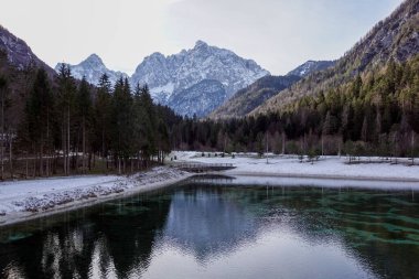 Barışçıl göl batımının güzel manzarası Fucine Tarvisio, İtalya 'da yeşil ormanlar ve arka planda karlı dağlar .