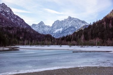 Barışçıl göl batımının güzel manzarası Fucine Tarvisio, İtalya 'da yeşil ormanlar ve arka planda karlı dağlar .