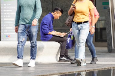 Milan, İtalya 4 Mayıs 2019: Kentin meydanındaki bankta otururken bilgisayar kullanan genç adam